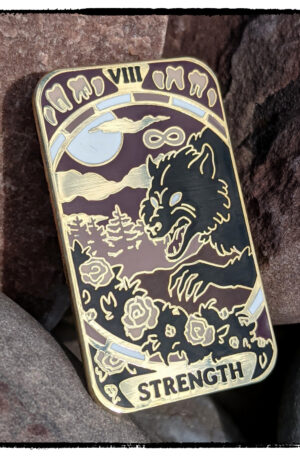 enamel pin of the Strength tarot card, featuring a werewolf plucking at rose bushes, tucked on some red rocks that match the reddish-purple of the pin