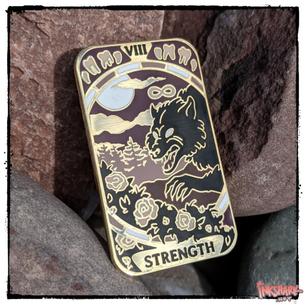 enamel pin of the Strength tarot card, featuring a werewolf plucking at rose bushes, tucked on some red rocks that match the reddish-purple of the pin