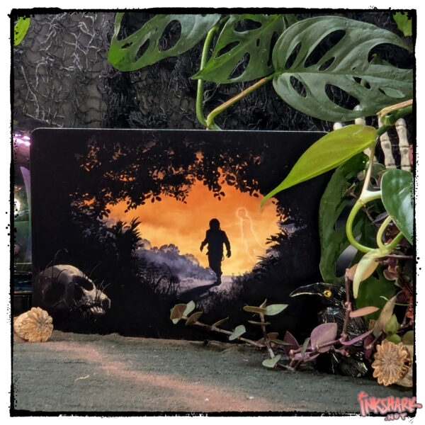 photo, postcard of a creepy scene where an astronaut walks through woods toward a hidden human skull, card is posed between tropical plant leaves, little figurines, and poppy seed pods