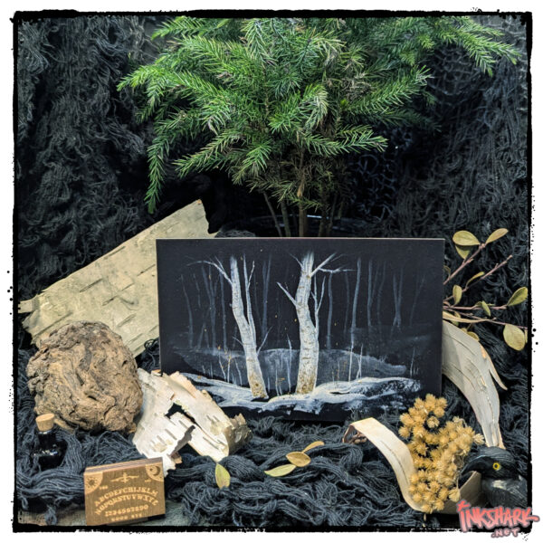 Postcard of two eerie winter birch trees; product is posed under a fir surrounded by woodland detritus, a carved stone crow, and the teeny-tiniest ouija board ever