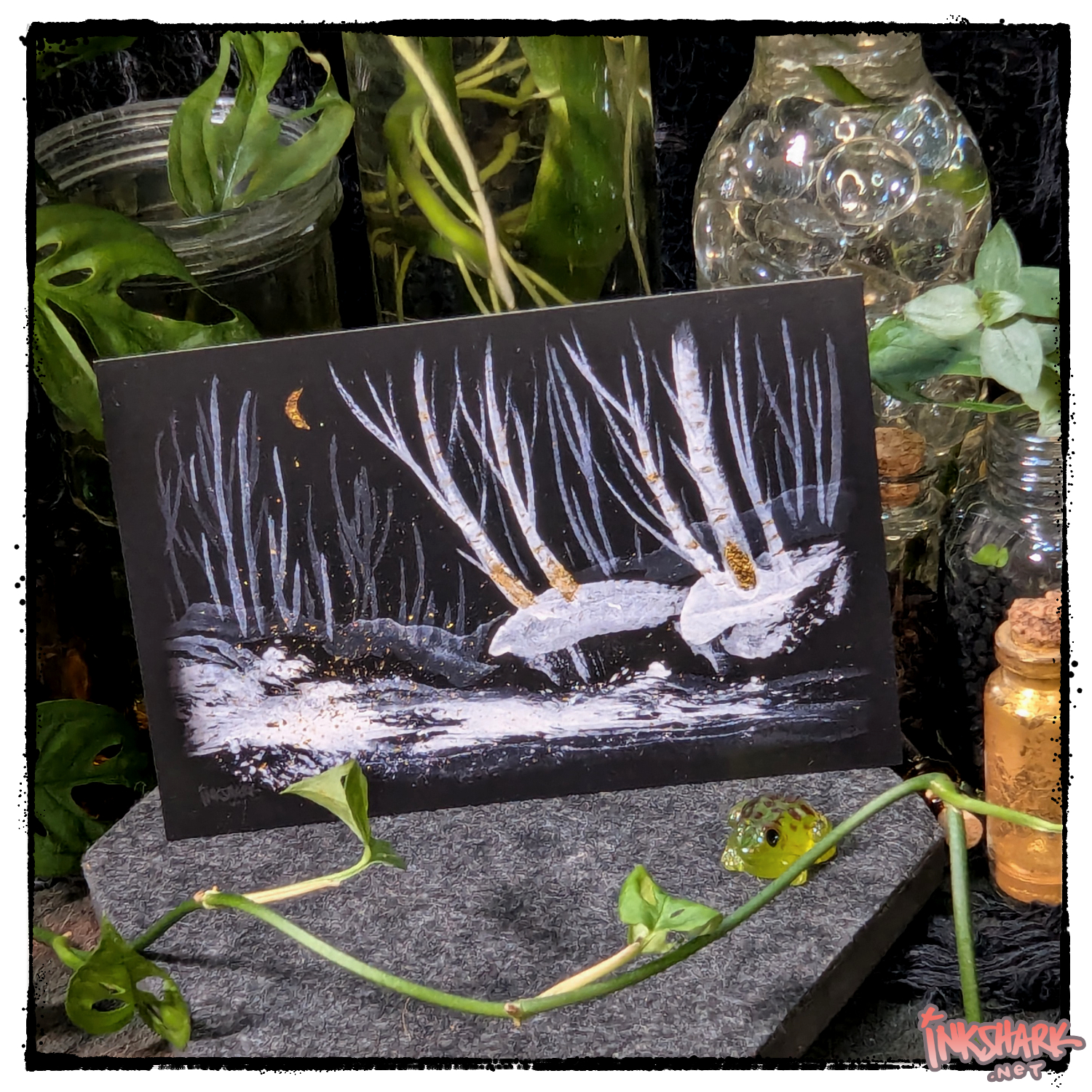 Postcard of eerie winter birch trees painted in gouache and gold ink, posed in front of witchy jars and bottles plus live plants