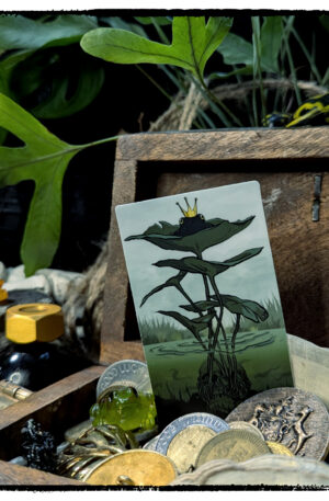 Sticker of a crowned frog perched on lily pads; product is tucked into a tiny wooden chest filled with coins