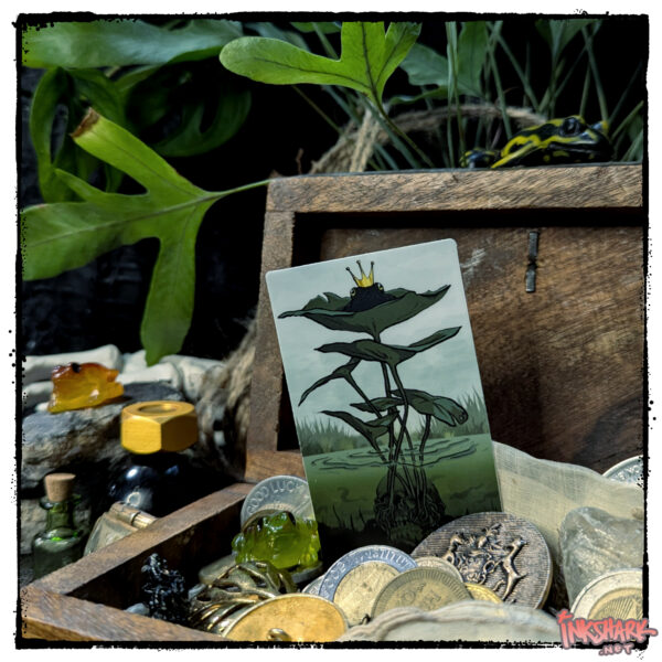 Sticker of a crowned frog perched on lily pads; product is tucked into a tiny wooden chest filled with coins