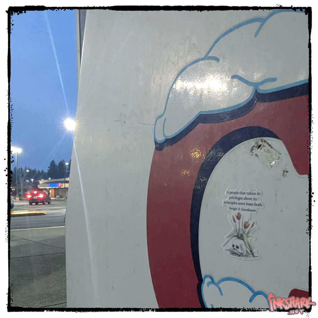 Photo of a sticker, has a drawing of serene tulips growing from a sleepy human skull. Text above reads: "A people that values its privileges above its principles soon loses both. — Dwight D. Eisenhower"